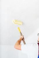 homem de macacão azul pintando a parede em branco com um rolo foto