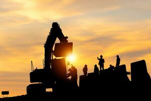 silhueta do engenheiro e trabalhador verificação projeto às construção site, engenheiro e construtores dentro capacetes discutindo em a infraestrutura construção local pôr do sol dentro tarde Tempo fundo foto