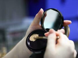 foto do uma mulher aplicando Maquiagem e preparando uma compactar mão espelho