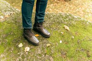 mulheres pés dentro couro outono chuteiras e jeans ficar de pé em a verde floresta musgo foto