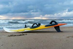 prancha de surfe deitado em a areia do a praia, mar ondas e a laranja prancha de surfe foto