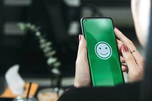 mulher detém uma Smartphone com feliz emoticons em a tela às uma restaurante. conceito do avaliando cliente satisfação às muito Boa nível do cliente serviço foto