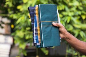 guardada algodão tecido lungi mão segurando com verde embaçado fundo. tradicional masculino moda estilo de vida dentro Bangladesh foto