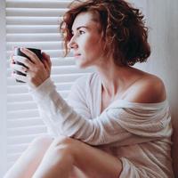 mulher pela janela com copo, relaxamento matinal luz suave movimento borrado foto