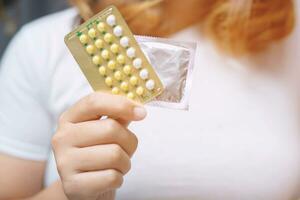 contraceptivo significa mulher mão segurando contraceptivo pílulas e preservativo em a cama. proteção, seguro sexo. contracepção, conceito nascimento ao controle. cópia de espaço foto