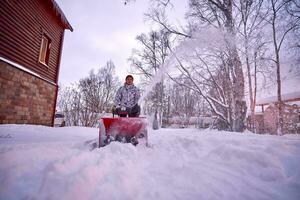 uma jovem homem limpa neve com uma neve ventilador dentro dele quintal. foto