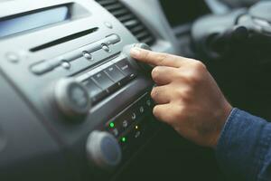 feche a mão aberta ouvindo o rádio do carro. motorista de carro mudando estações de rádio de botão giratório em seu sistema multimídia do veículo. moderno sistema estéreo de áudio com tela de toque. conceito de transporte e veículo foto