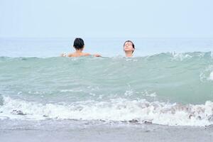 uma Garoto e uma menina estão tendo Diversão jogando dentro a mar dentro a ondas. foto