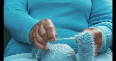 uma mulher com tricô dentro dela mãos. a mãos do a velho mulher às bordado. uma mulher dentro azul dissolve uma de lã lenço. foto