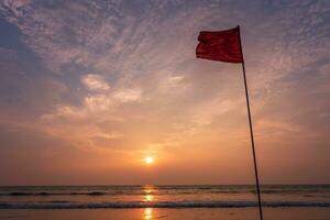 vermelho bandeira em de praia em mar ou oceano às pôr do sol Como símbolo do perigo. a mar Estado é considerado perigoso e natação é Entrada. foto