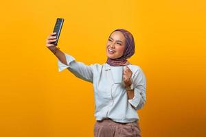Mulher asiática alegre usando celular fazendo selfie enquanto segura a caneca