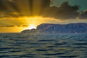 Visão a partir de a mar para a oeste capa dentro Noruega dentro brilho do sol e pesado nuvens. panorama foto