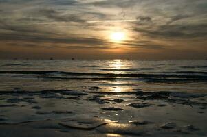 pôr do sol, pequeno Rocha às baixo maré dentro frente do a iluminado mar. báltico mar. foto