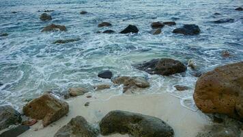 Visão lindo tropical de praia com rochas, coral, ondas, azul mar, oceano, azul céu, areia de praia e nuvens em marina de praia dentro Kalianda, lampung. popular período de férias do turismo dentro sumatra ilha, Indonésia foto