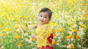 pequeno fofa menina vestindo amarelo balinesa vestir jogando dentro amarelo e branco flor jardim foto