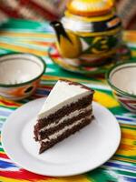 sobremesa chocolate bolo com branco manteiga creme dentro oriental estilo em uma telhado com uma chaleira e uma copo para chá. foto