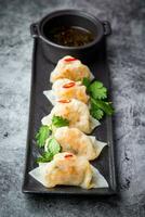 ásia dumplings com soja molho, Pimenta pimentas e ervas em uma Sombrio fundo lado Visão foto