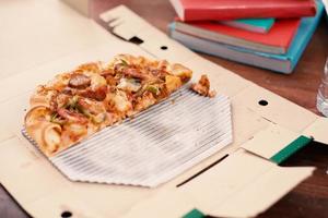pedaço de pizza na mesa. pizza na mesa com livros e bebidas foto