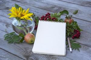 o bloco de notas em branco sobre uma mesa de madeira, lugar para texto. flores e frutos foto