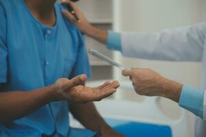 fechar acima do médico sentado em de cabeceira do masculino paciente dentro hospital foto