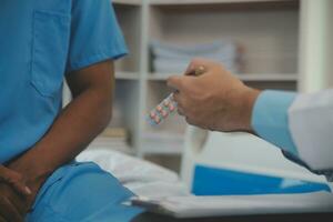 fechar acima do médico sentado em de cabeceira do masculino paciente dentro hospital foto