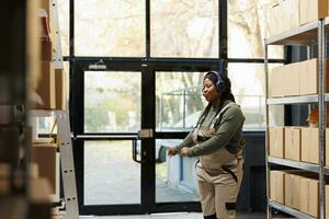 sorridente almoxarifado Gerente tendo Diversão dentro armazém, dançando e ouvindo música enquanto trabalhando às clientes ordens. pequeno o negócio empregado trabalhando dentro armazém, preparando pacotes foto