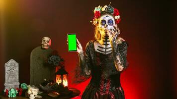 arrepiante fêmea modelo segurando tela verde em Smartphone, usando Móvel telefone com isolado brincar modelo. mulher vestido Como santa muerte mostrando em branco croma chave copyspace mostrar. foto