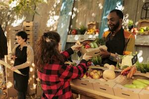 jovem amigáveis agricultor servindo cliente com vários produzir e vendendo caseiro Fazenda legumes às local Comida mercado. fêmea cliente comprando fresco orgânico frutas e vegetais, agricultura nutrição. foto