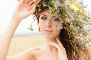 lindo mulher com uma guirlanda em dela cabeça sentado dentro uma campo dentro flores foto