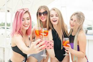 quatro atraente meninas em repouso em a de praia bar, beber uma refrescante coquetel foto