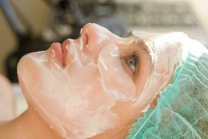 fêmea cosmetologista fazer Cosmético facial mascarar para a fêmea cliente foto