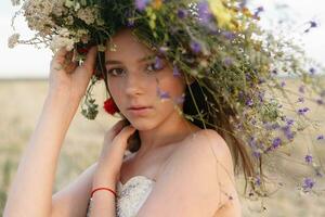 lindo mulher com uma guirlanda em dela cabeça sentado dentro uma campo dentro flores foto