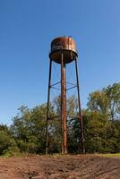uma lindo água torre é conjunto por aí a abandonado área. isto oxidado metal estrutura carrinhos alta contra uma azul céu. foto