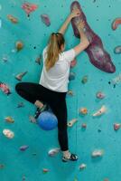 jovem mulher escalada acima em prática parede dentro Academia foto