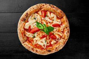 tradicional pizza margherita com pelati molho, mussarela, tomates e manjericão em Preto de madeira superfície foto