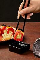 fêmea mão segurando vermelho arroz Sushi lista com atum com pauzinhos sobre soja molho foto