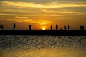 silhueta do uma grupo do pessoas caminhando em a de praia às pôr do sol. foto