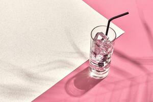 vidro do mineral água com gelo em Rosa e branco fundo com sombra a partir de uma Palma folha foto