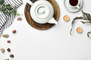 uma branco porcelana chaleira em uma de madeira borda e uma branco copo com chá em uma mesa. topo visualizar. cópia de espaço. foto