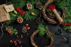 faço uma Natal guirlanda com seu próprio mãos. abeto filial, Natal guirlanda e presentes em uma Preto de madeira fundo foto