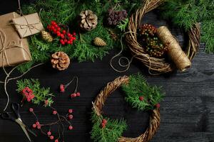 faço uma Natal guirlanda com seu próprio mãos. abeto filial, Natal guirlanda e presentes em uma Preto de madeira fundo foto