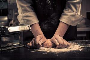 a chefe de cozinha faz massa para massa em uma de madeira mesa foto