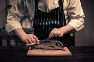 chefe de cozinha corte a peixe em uma borda foto