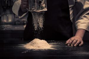 a chefe de cozinha mãos estão caindo farinha sobre uma de madeira mesa foto