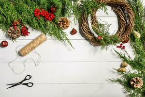 faço uma Natal guirlanda com seu próprio mãos. abeto filial, Natal guirlanda e presentes em uma branco de madeira fundo foto