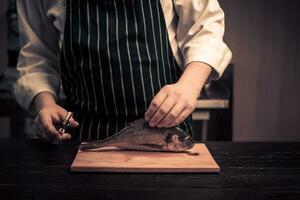 chefe de cozinha corte a peixe em uma borda foto