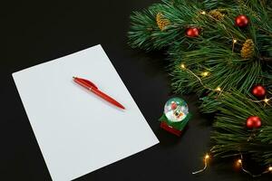 vermelho Natal bolas e caderno deitado perto verde abeto ramo em Preto fundo topo visualizar. espaço para texto foto