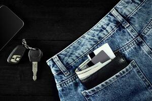 dinheiro, débito cartão e crédito cartão estão dentro bolso do azul jeans, carro chaves, inteligente em de madeira fundo com cópia de espaço. foto
