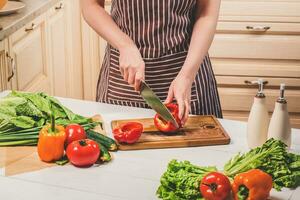 jovem mulher cozinhando dentro a cozinha às lar. uma mulher cortes uma Pimenta e legumes com uma faca. foto
