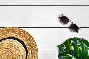 branco de madeira fundo com Palha chapéu, oculos de sol e verde folha. verão férias, recorrer e lazer conceito. fechar acima, cópia de espaço foto